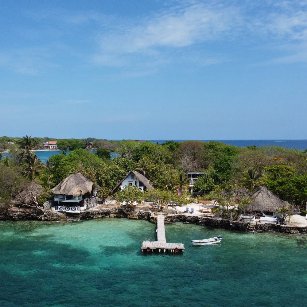 Tropical island with thatched-roof buildings, a dock, and clear blue water.