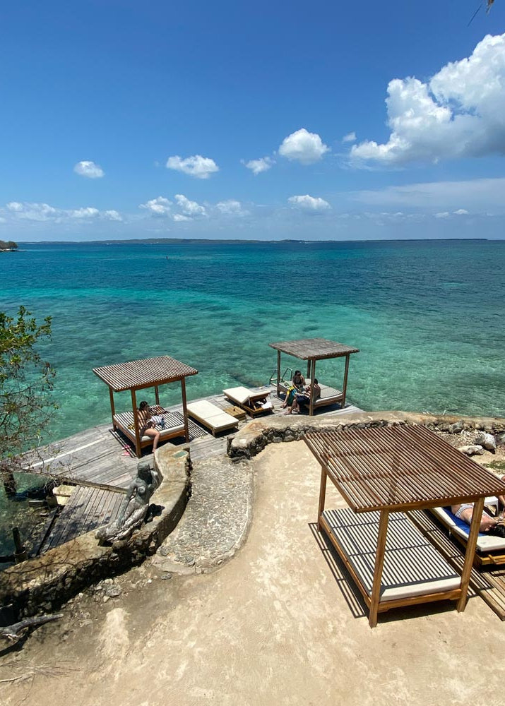 Beachside relaxation area with lounge chairs and wooden structures overlooking clear blue water.