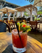Cocktail with lime and cherry garnish on a wooden table outdoors.