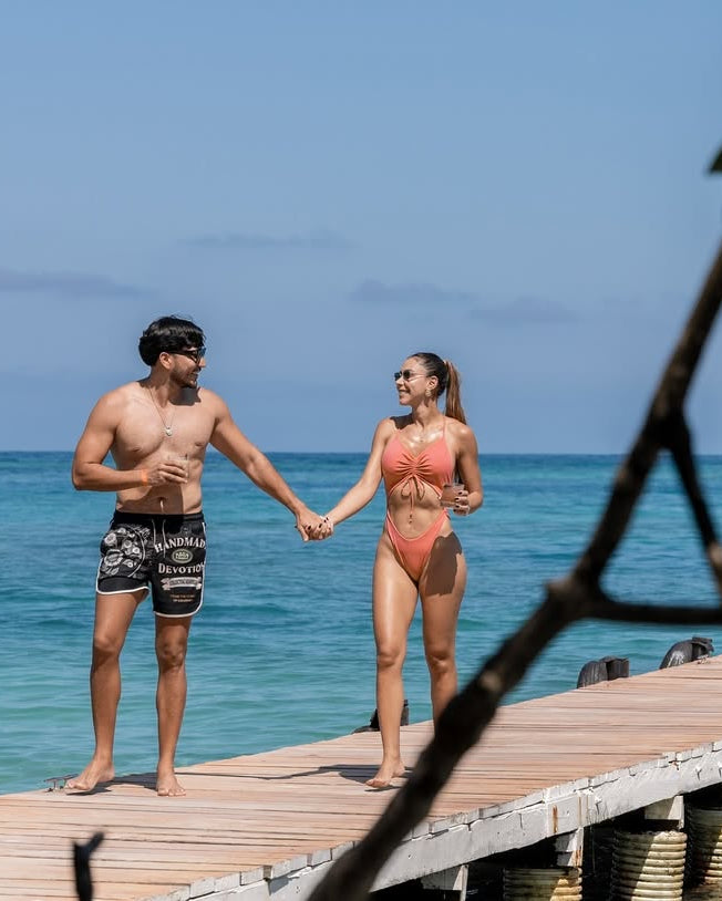 Two people holding hands on a wooden dock by the ocean.