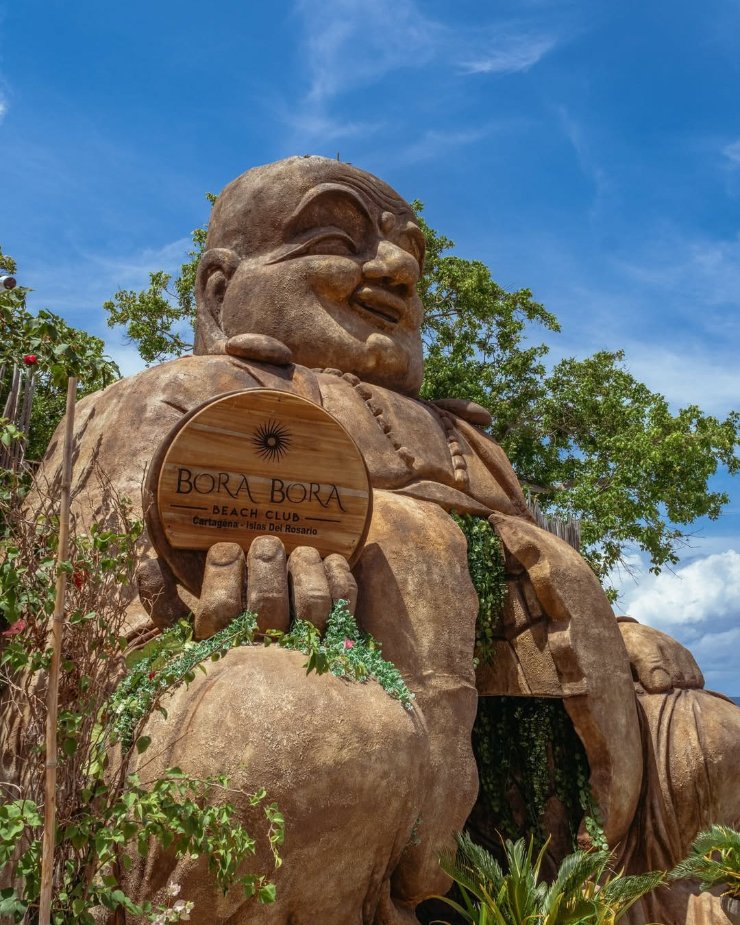 Large stone statue with a sign reading 'Bora Bora' against a blue sky.