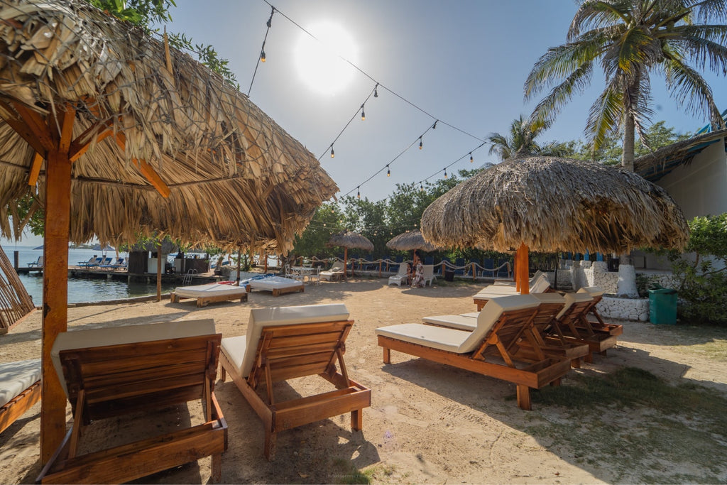 Beachside lounge area with thatched umbrellas and wooden chairs near a body of water.