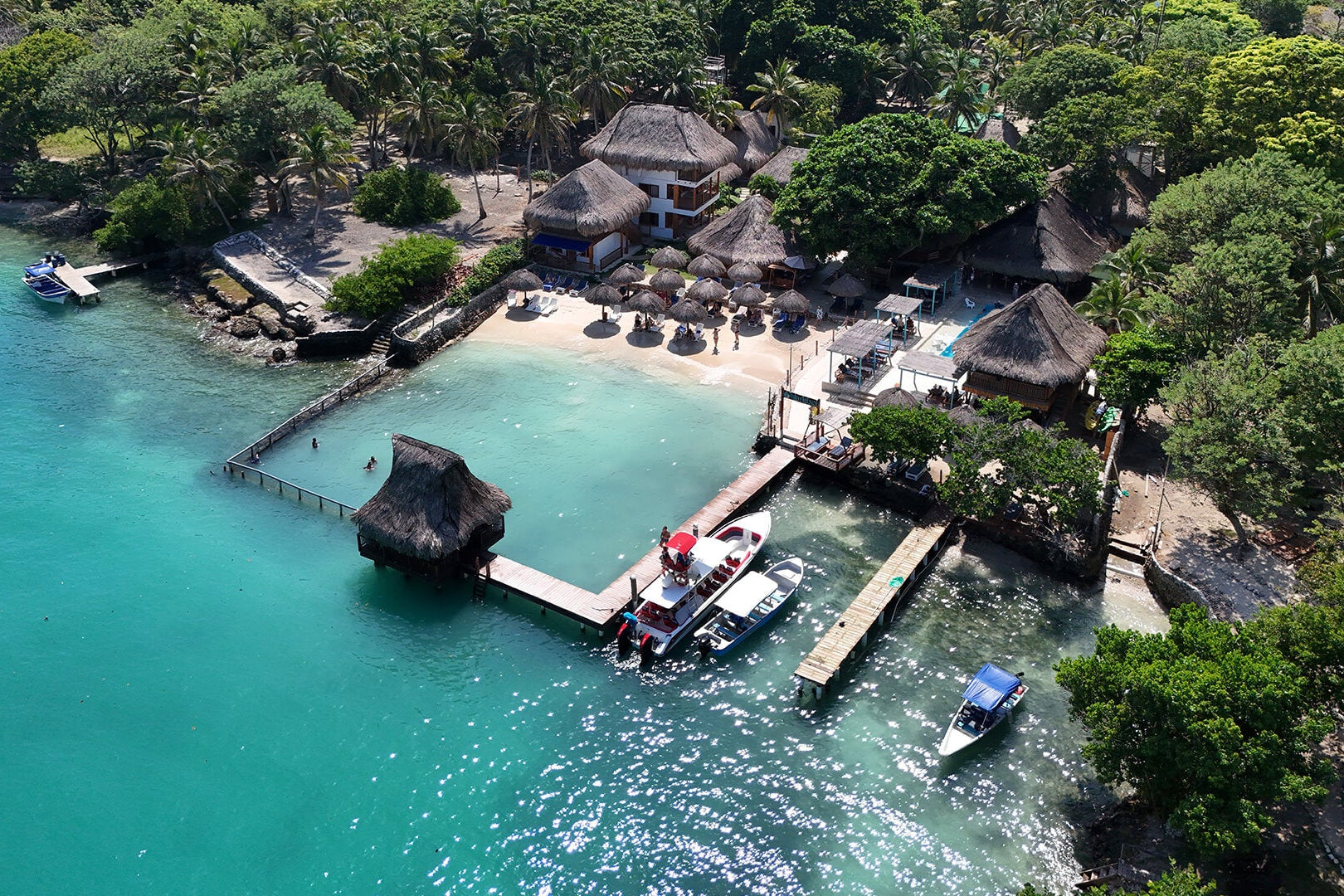 Aerial view of a tropical island with a dock and boats near turquoise waters.