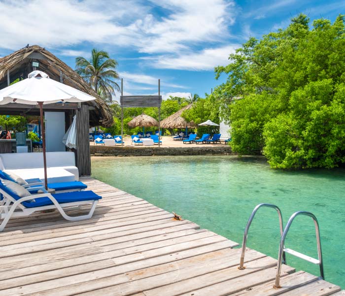 Tropical resort with wooden dock, lounge chairs, and thatched umbrellas by a clear blue lagoon.