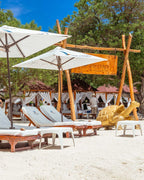 Beachside relaxation area with lounge chairs, umbrellas, and a wooden sculpture on a sandy beach.