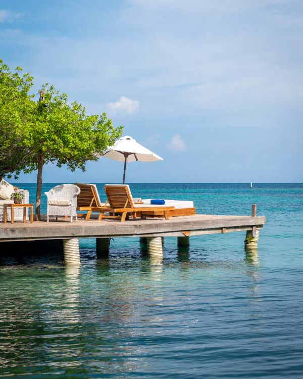 Wooden dock with lounge chairs and an umbrella over calm blue water and sky.