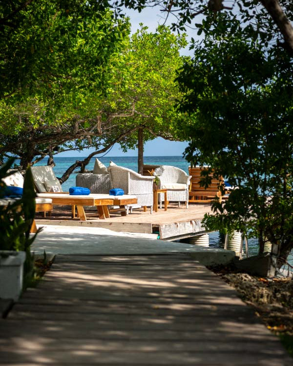 Outdoor seating area with chairs and tables on a wooden deck by the water, surrounded by trees.